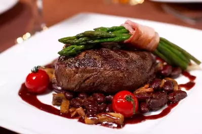 A tasty steak with beans, tomatoes, and asparagus wrapped in bacon.