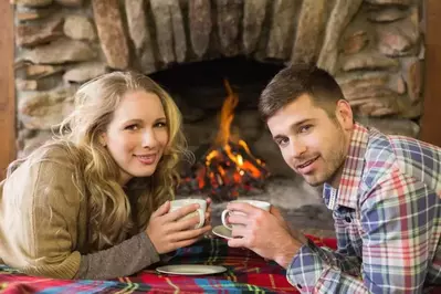 Couple drinking coffee beside the fireplace.