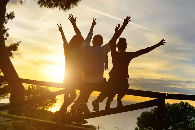 Rear view of three best friend travelers putting their hands up at sunset.