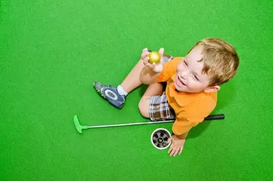toddler holding golf ball sitting next to hole