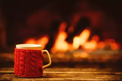 A mug with a wool koozie in front of a fireplace.