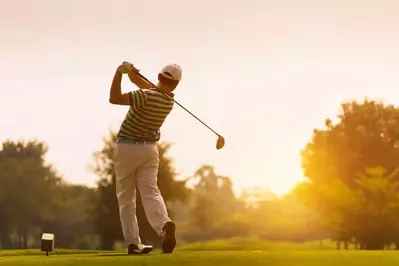 A man playing golf on a beautiful course in the late afternoon.